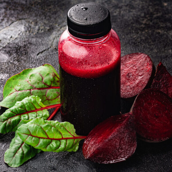 Fresh squeezed beet juice in bottle among leaves and beetroot chunks, selective focus, copy space