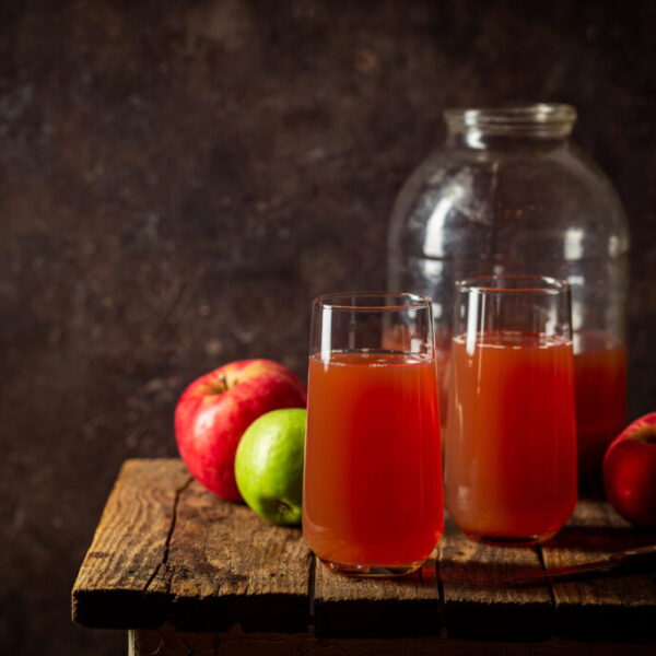 Glass of fresh apple juice and red apples on dark wooden background