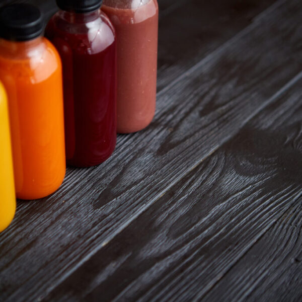 Colorful bottles filled with fresh fruit and vegetable juice or smoothie. Placed in row on black wooden table.