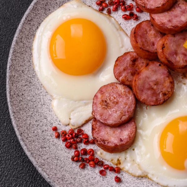 Delicious nutritious breakfast with fried eggs, sausage, steamed vegetables with salt, spices and herbs on a dark concrete background