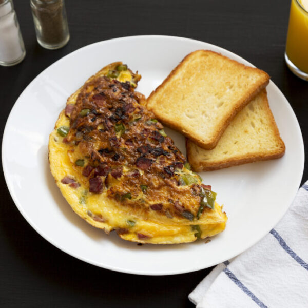 Homemade Denver Omelette on a white plate on a black background, low angle view.